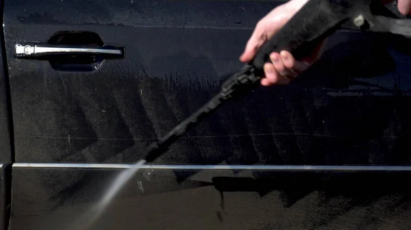 Lava la suciedad de un coche con un primer plano de chorro de agua a alta presión. Detergente especial para lavado de autos. Lava un coche delante de la casa . — Foto de Stock