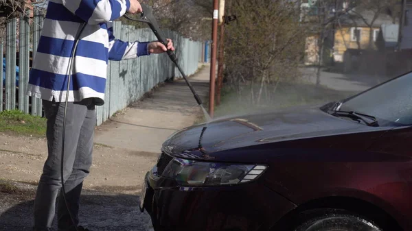 Un hombre lava la tierra de un coche con un chorro de agua de alta presión. Detergente especial para lavado de autos. Lava un coche delante de la casa . — Foto de Stock