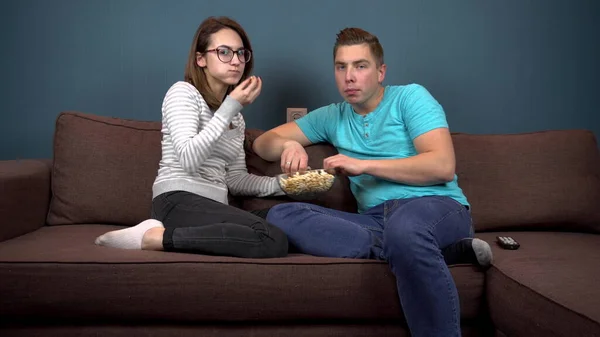 Fiatal férfi és nő tévézik és popcornt eszik. Egy pattogatott kukoricás tányérért harcoló pár. Nézd figyelmesen a TV-t. — Stock Fotó