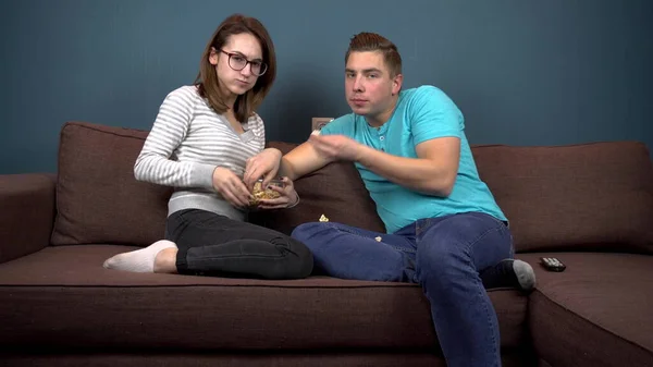 Fiatal férfi és nő tévézik és popcornt eszik. Egy pattogatott kukoricás tányérért harcoló pár. Nézd figyelmesen a TV-t. — Stock Fotó
