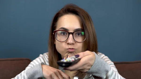 Una joven con gafas come papas fritas y ve televisión. Close-up girl come activamente chips y canales de interruptores — Foto de Stock