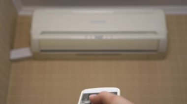 Odadaki ısıyı ayarlamak için evdeki klima. Bir kadın uzaktan kumandayla klimayı açar. Yakın plan. Klima bulanık