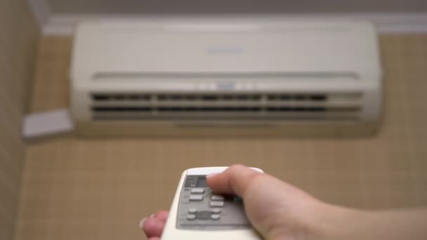Légkondi a házban, hogy állítsa be a hőmérsékletet a szobában. Egy nő kikapcsolja a légkondit a távirányítóval. Közelkép. Homályos légkondicionáló berendezés — Stock videók