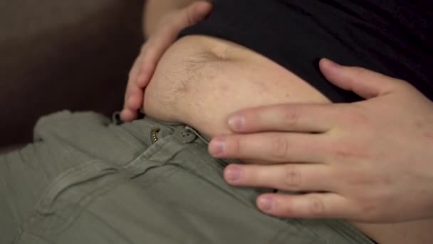 Un giovanotto batte le mani sul suo stomaco grasso. Aumento di peso in eccesso in quarantena. La pancia trema da vicino. Rallentatore. — Video Stock