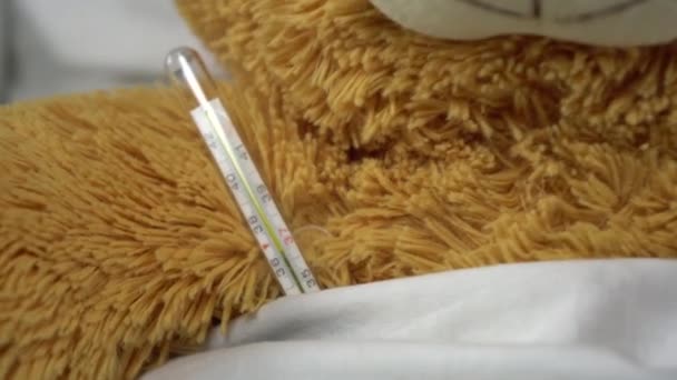 Un ours en peluche mesure la température avec un thermomètre au mercure. L'ours repose dans son lit. — Video