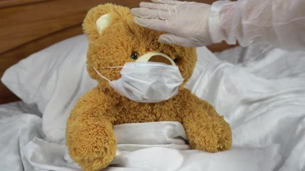 Teddy bear measure the temperature by hand. The doctor makes a measurement of temperature by applying a hand to his forehead. The doctor shows a thumbs up means that the temperature is elevated. — Stock Video