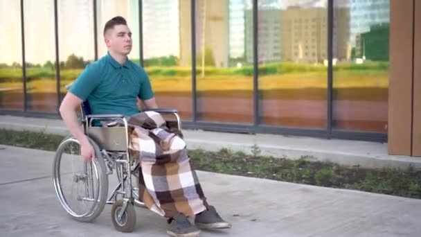 Ein junger Mann sitzt im Rollstuhl und erleidet einen Herzinfarkt. Ein Mann im Rollstuhl vor dem Hintergrund eines gläsernen Gebäudes fasst sich ein Herz. Spezielle Transportmittel für Behinderte. — Stockvideo