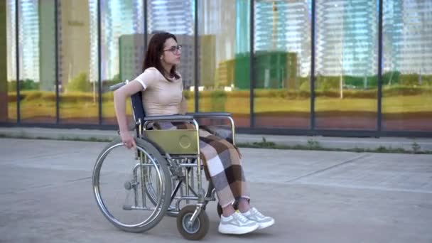 휠체어를 탄 젊은 여성. 한 소녀가 휘일 체어 를 타고 유리 건물을 배경으로 달린다. 신체장애자를 위한 특별 수송 수단. — 비디오