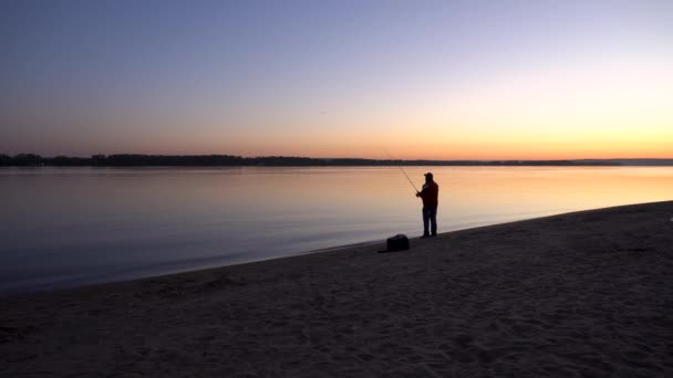 Bir adam gün doğumunda nehir kenarında balık tutuyor. Sarı güneş ufuktan yükseliyor. Bir balıkçının silueti.. — Stok video