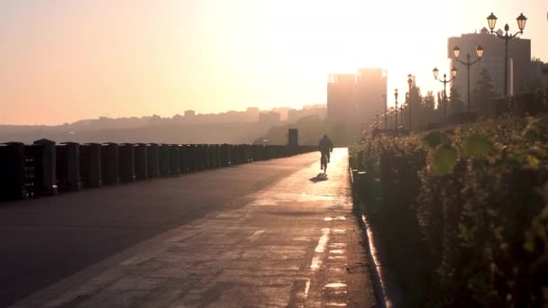 Un uomo va in bicicletta lungo il lungomare per incontrare l'alba. Silhouette di un uomo in bicicletta. — Video Stock