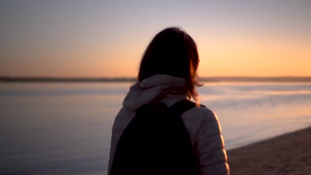 Een jonge vrouw loopt bij zonsopgang langs het strand langs de rivier. Silhouet van een meisje. Gaat de dageraad tegemoet. — Stockvideo