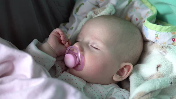 아기는 유모차를 타고 입 안에서 고무젖꼭지를 물고 자고 있다. 얼굴을 감아. — 스톡 사진