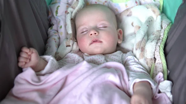 아기는 유모차를 타고 입 안에서 고무젖꼭지를 물고 자고 있다. 얼굴을 감아. — 스톡 사진