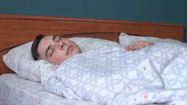 Pod peřinou spí mladý muž. Muž leží v posteli ve svém pokoji. — Stock fotografie