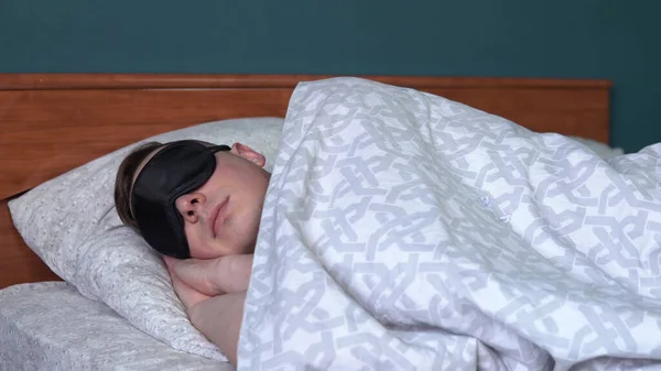 Um jovem dorme com uma máscara de sono. Um homem jaz na cama em seu quarto . — Fotografia de Stock