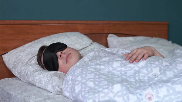 Um jovem dorme com uma máscara de sono. Um homem jaz na cama em seu quarto . — Fotografia de Stock