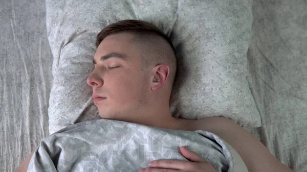 Um jovem está a dormir debaixo dos lençóis. Um homem está deitado na cama no quarto. Vista de cima . — Fotografia de Stock