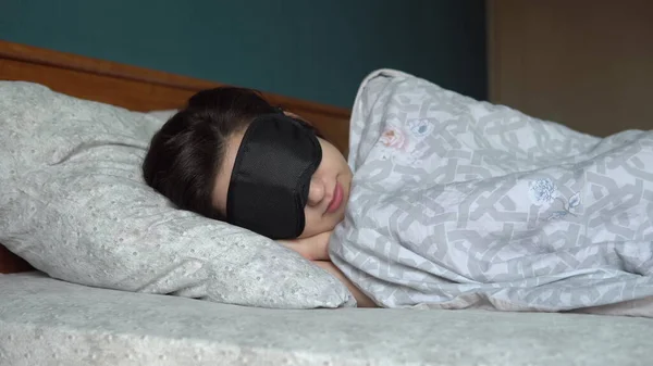 Uma jovem dorme com uma máscara de sono. Uma menina jaz na cama em seu quarto . — Fotografia de Stock