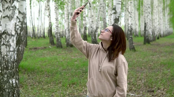 Μια νεαρή γυναίκα ψάχνει για ένα δίκτυο κινητής τηλεφωνίας σε ένα δάσος από σημύδες. Ένα κορίτσι μιλάει στο τηλέφωνο, αλλά η σύνδεση διακόπτεται. Η γυναίκα είναι νευρική.. — Φωτογραφία Αρχείου