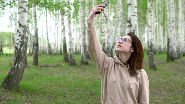 Una joven está buscando una red celular en un bosque de abedules. Una chica está hablando por teléfono, pero la conexión se interrumpe. La mujer está nerviosa. . —  Fotos de Stock