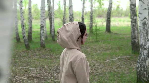 Una giovane donna cammina attraverso una foresta di betulle. Una ragazza cammina nel parco. Vista attraverso gli alberi. — Foto Stock