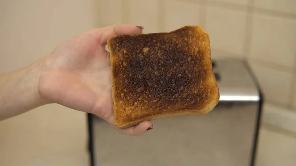 Woman holds burnt toast in her hand — Stock Photo, Image