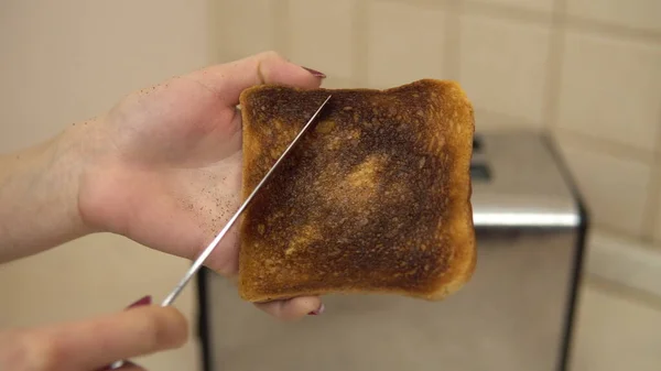 Frau säubert die Asche mit einem verbrannten Toast mit einem Messer. Toastbrot im Toaster — Stockfoto