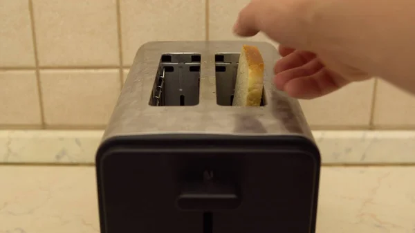 Un hombre pone pan en una tostadora. El pan está frito. Se está preparando la comida para el desayuno. Electrodomésticos en la cocina — Foto de Stock