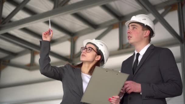 Ten muž ten projekt neschvaluje. Mladý muž a žena v helmách s dokumenty na staveništi. Šéfové v oblecích diskutují o architektonickém projektu. Lidé se rozhlížejí. — Stock video