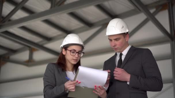 Young man and woman in helmets with documents at a construction site. Businessmen in suits conclude an agreement. A man signed documents. — Stock Video