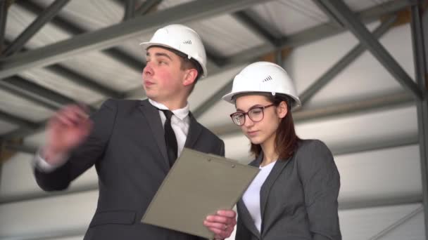 La femme approuve le projet. Jeune homme et femme casques avec documents sur un chantier de construction. Les patrons en costume discutent d'un projet d'architecture. Les gens regardent autour. — Video