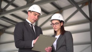 Kadın projeyi onaylamıyor. İnşaat alanında kasklı genç bir adam ve kadın. Takım elbiseli patronlar bir mimarlık projesini tartışıyorlar. İnsanlar etrafına bakıyor..