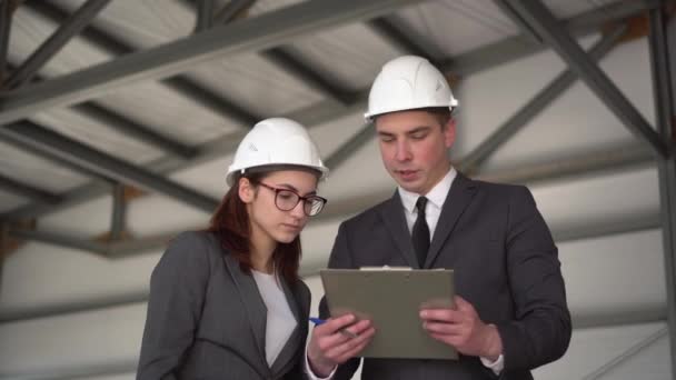 Jeune homme et femme casques avec documents sur un chantier de construction. Les hommes d'affaires en costume concluent un accord. Une femme a signé des documents. — Video