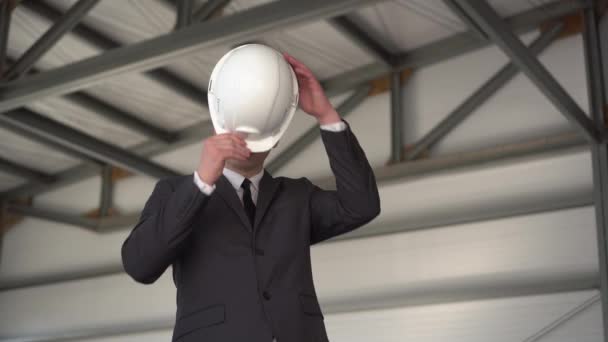 Un jeune homme porte un casque de protection et montre un pouce sur un chantier de construction. Le patron en costume regarde la caméra.. — Video