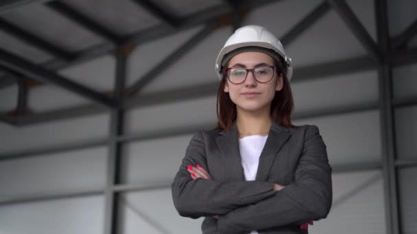 A young woman in a protective helmet crossed her arms and stands at a construction site. The boss woman in a suit looks at the camera. — Stock Video