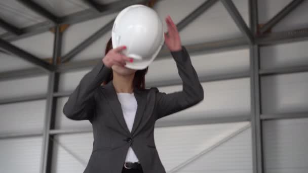 Eine junge Frau setzt sich einen Schutzhelm auf und zeigt auf einer Baustelle einen Daumen. Der Chef im Anzug blickt in die Kamera. — Stockvideo