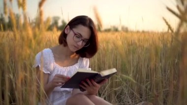Genç bir kadın sarı bir tarlada kitap okuyor. Bir kız elinde kitapla buğday tarlasında bir elbisede oturuyor..