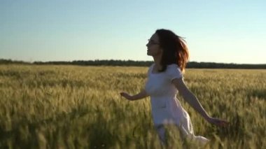 Beyaz elbiseli genç bir kadın tarlada koşuyor. Yeşil buğday tarlasında mutlu bir kız. Yavaş çekim.
