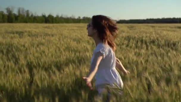 Młoda kobieta biegnie przez boisko w białej sukience. Szczęśliwa dziewczyna na zielonym polu pszenicy. Zwolniony ruch. — Wideo stockowe