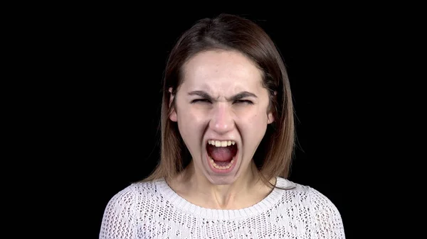 Una mujer joven muestra emociones de ira en su cara. Mujer grita de rabia sobre un fondo negro . — Foto de Stock