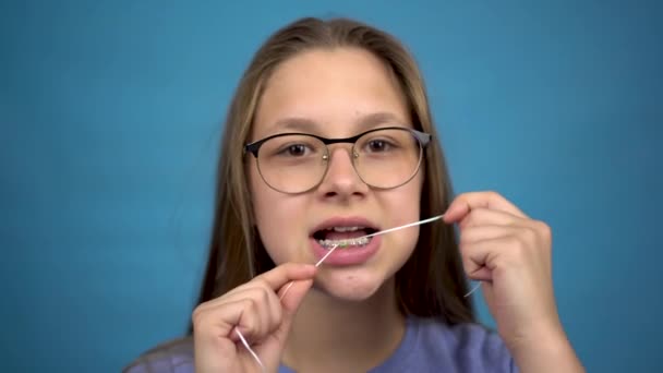 Fille avec bretelles brossant vos dents avec de la soie dentaire. Une fille avec des accolades colorées sur ses dents garde ses dents propres. — Video