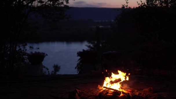 Una hoguera arde en medio de la noche. Fuego en el fondo del río y las montañas. — Vídeos de Stock