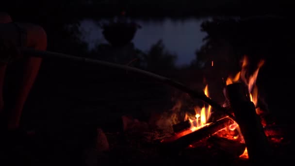 L'homme redresse les charbons dans le feu. Le feu brûle au milieu de la nuit gros plan. — Video