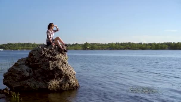 Egy fiatal nő ül egy kövön a folyónál, és csodálja a természetet. Lány a természetben. — Stock videók