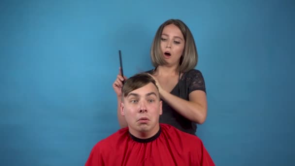 Kadeřník účes rozmazlený mladý muž. Mladá žena si omylem ostříhala velkou část vlasů na mužově hlavě. Na modrém pozadí. — Stock video
