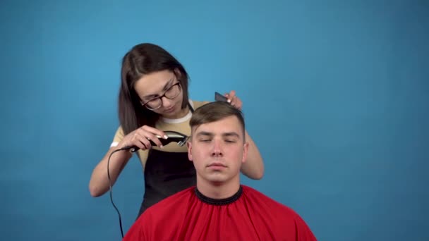 Cabeleireiro penteado mimado jovem. Uma jovem acidentalmente cortou muito do cabelo na cabeça do homem. Em um fundo azul . — Vídeo de Stock