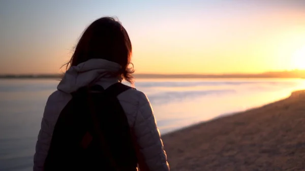 Eine junge Frau geht bei Sonnenaufgang am Strand entlang des Flusses. Silhouette eines Mädchens. Geht der Morgendämmerung entgegen. — Stockfoto