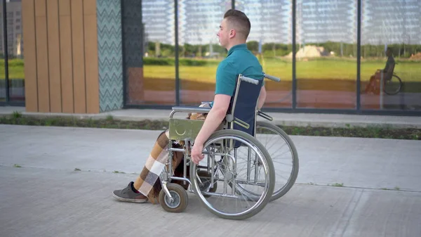 Mladý muž na vozíčku. Muž jede na invalidním vozíku na pozadí skleněné budovy. Speciální přeprava pro zdravotně postižené. — Stock fotografie