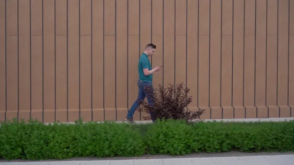 Un joven va con un teléfono en la mano. Un hombre camina cerca del edificio y lleva la correspondencia en un teléfono inteligente. —  Fotos de Stock