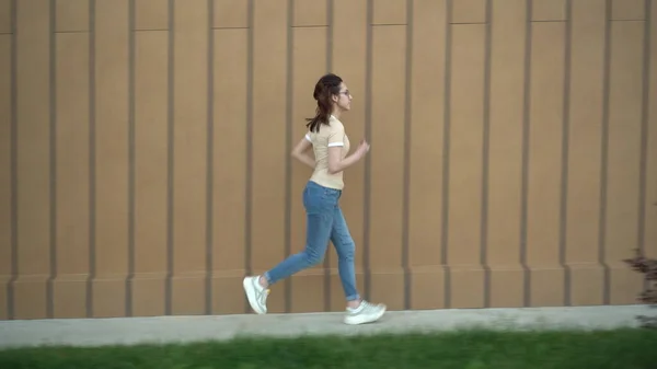 Eine junge Frau läuft in der Nähe eines Einkaufszentrums. Das Mädchen ist spät dran und rennt. Freizeitkleidung. — Stockfoto